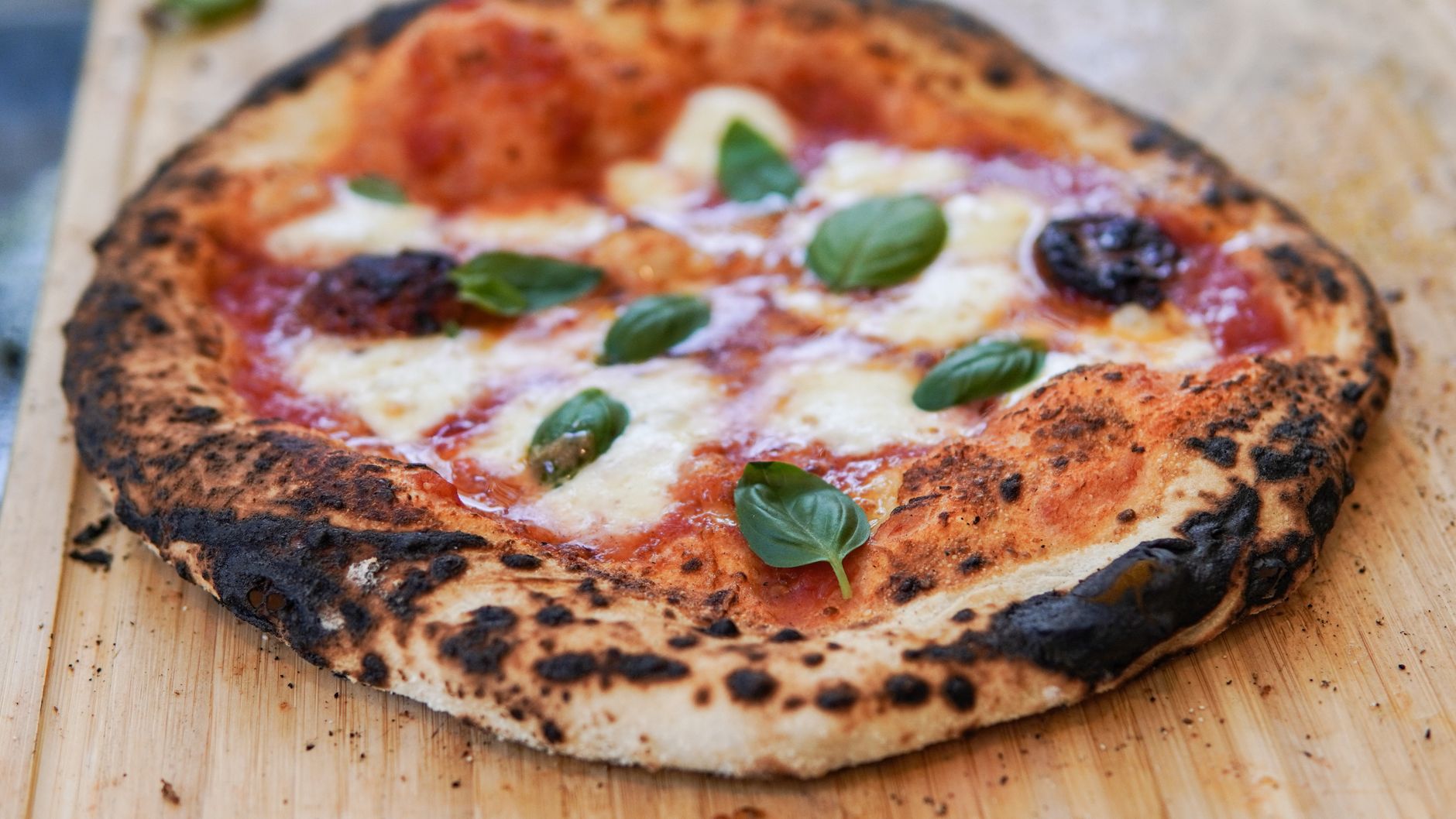 Pizza margherita napolitaine à la croûte gonflée et tachetée, sur une planche de bois, garnie de basilic frais.